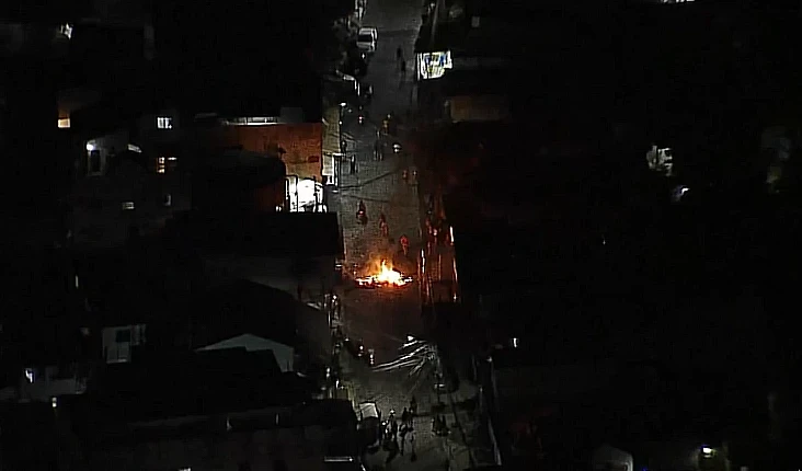 **Legenda:** Vista aérea mostra barricada em chamas na Cidade de Deus, RJ, durante operação policial em resposta a ação de traficantes.