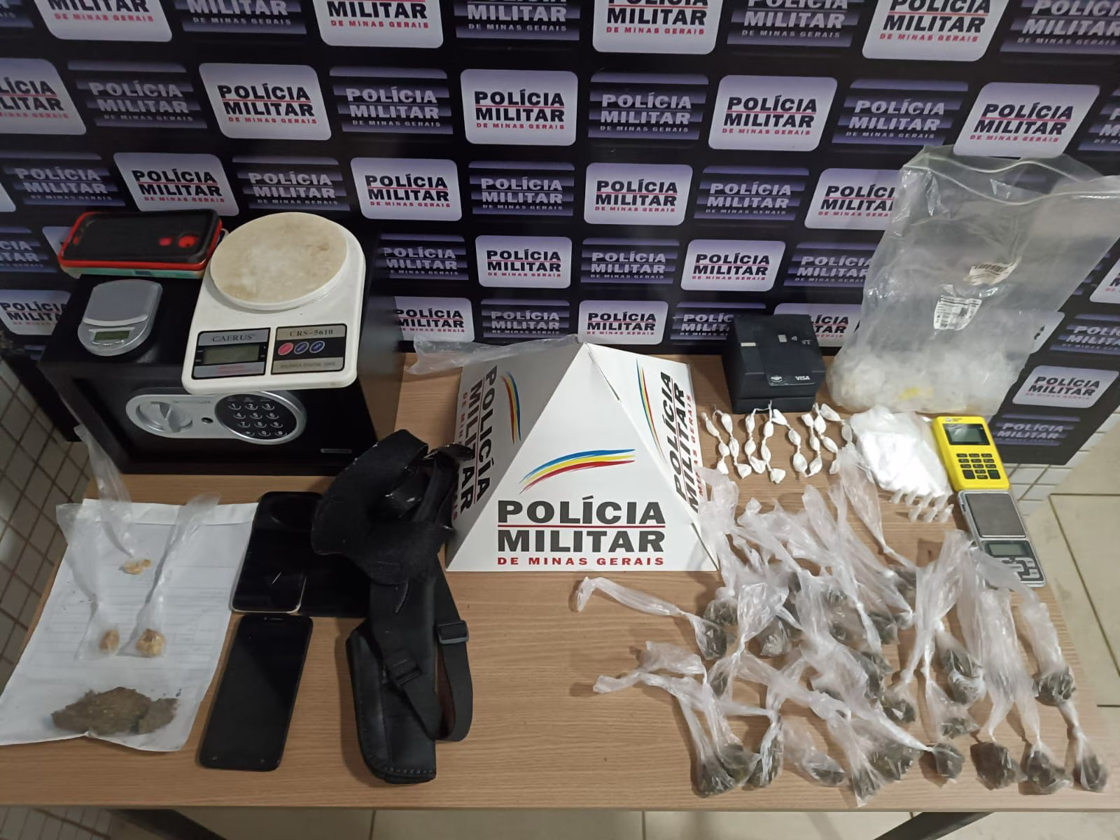 Na residência, os policiais descobriram 32 porções de maconha, 26 papelotes e sete pinos de cocaína, além de uma balança de precisão, R$100 em dinheiro, uma maquita de cartão, itens para embalar entorpecentes e um celular.